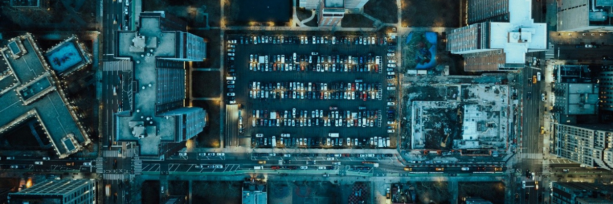 A photograph shows a birds-eye perspective on a very urban and modern city landscape, with a parking lot at the center, surrounded by several skyscrapers